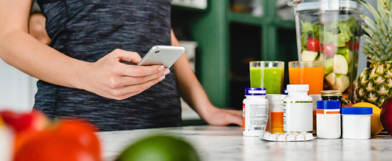 Young woman searching info about food supplements on her phone with fruits and additives on the table